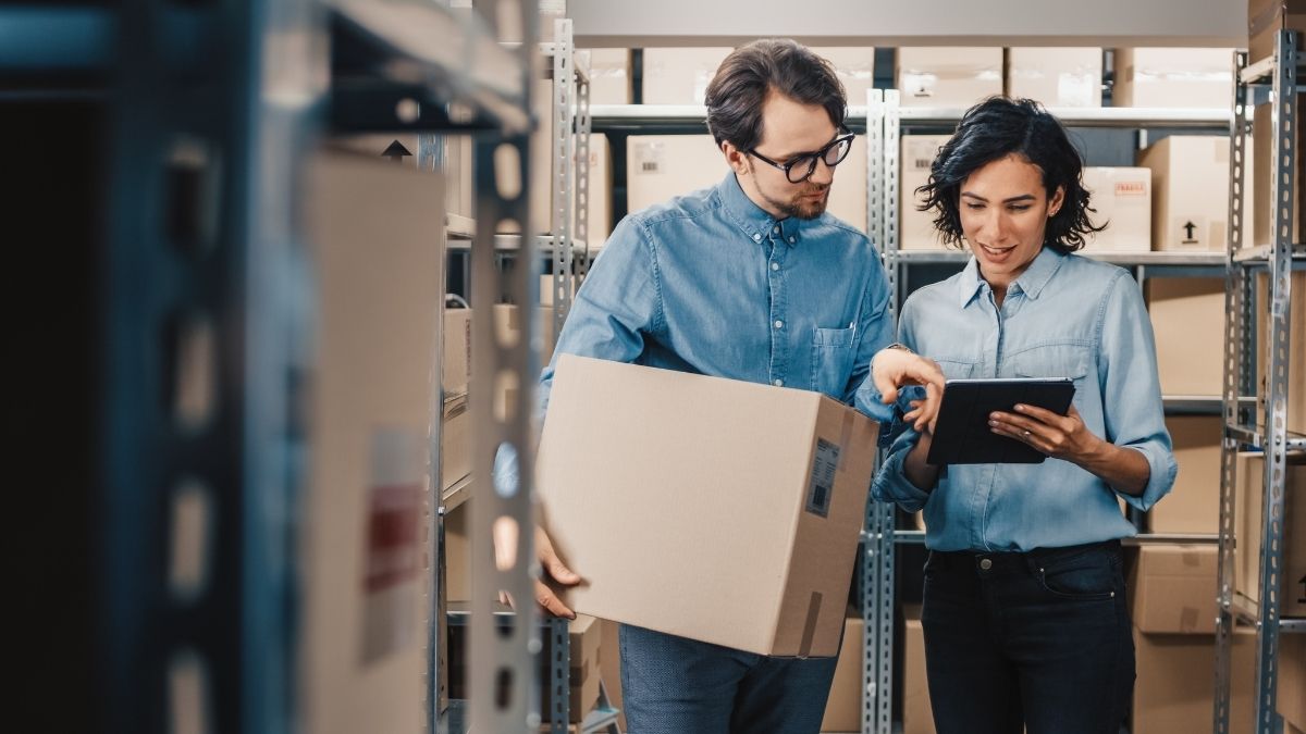 Two coworkers looking at a tablet, one holding a box