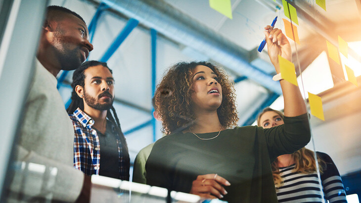 Coworkers writing on a clear dry erase board.